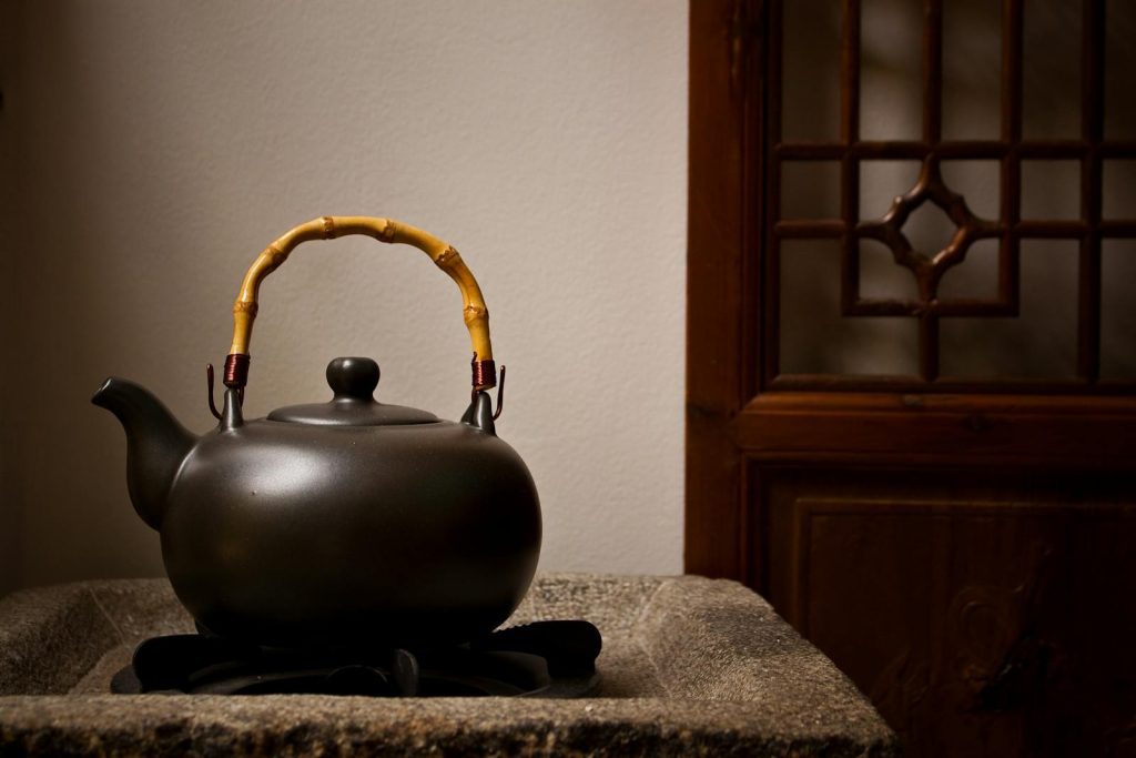 A black teapot with bamboo handle on a rustic stone stove, creating a serene kitchen atmosphere.