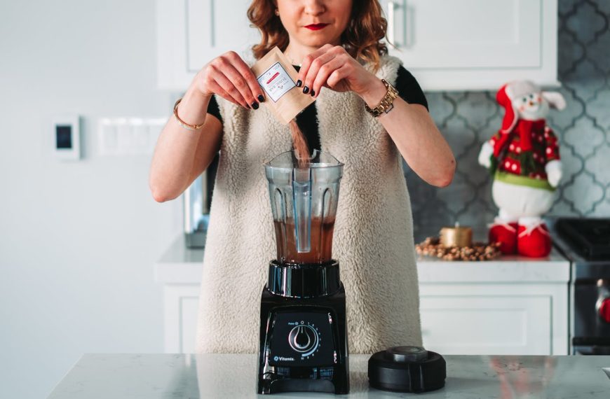 A woman pours a sachet into a blender in a festive kitchen setting.