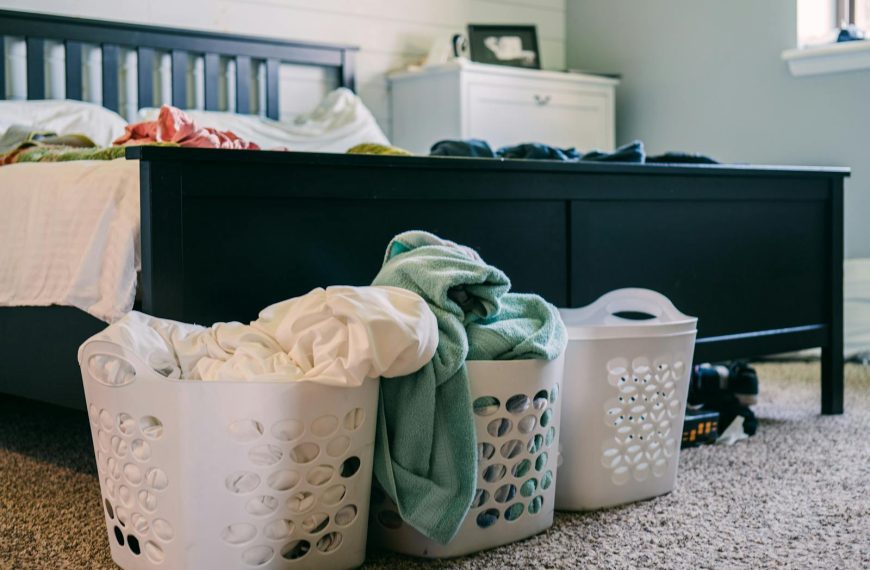 A cozy bedroom scene featuring laundry baskets filled with clothing, placed on a carpeted floor.