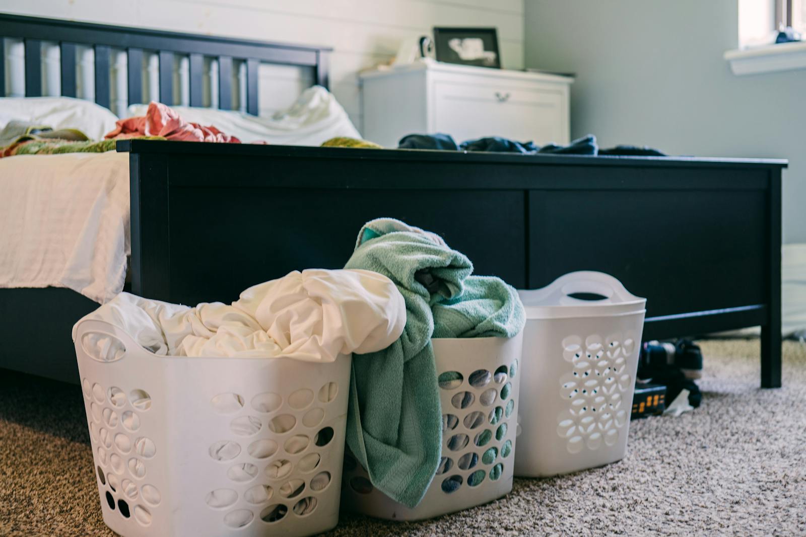 A cozy bedroom scene featuring laundry baskets filled with clothing, placed on a carpeted floor.