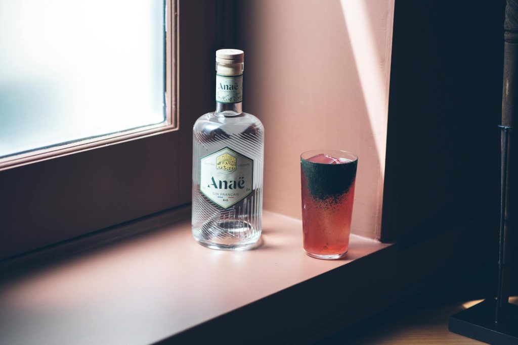 Stylish Anaé gin bottle with a vibrant cocktail on a windowsill, creating a refreshing ambiance.