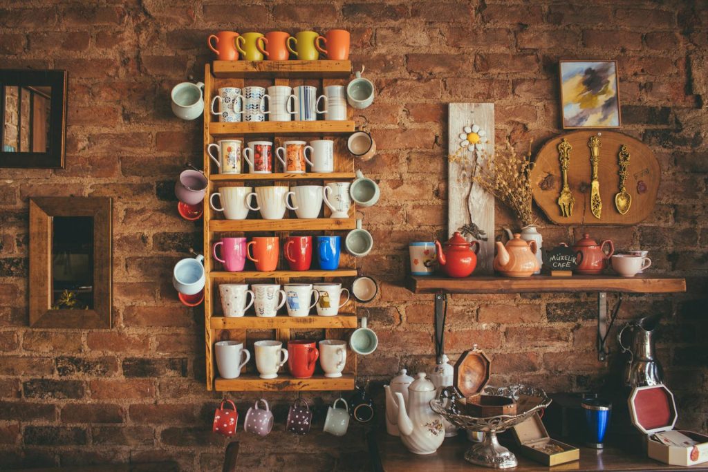 A collection of colorful vintage mugs and teapots displayed on shelves against a rustic brick wall.