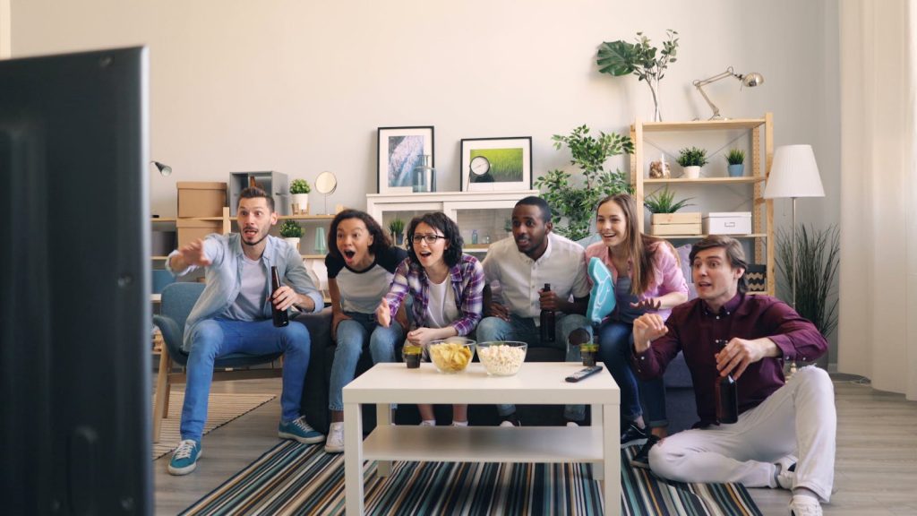 A lively group of diverse friends cheering while watching a sports game together in a cozy living room.