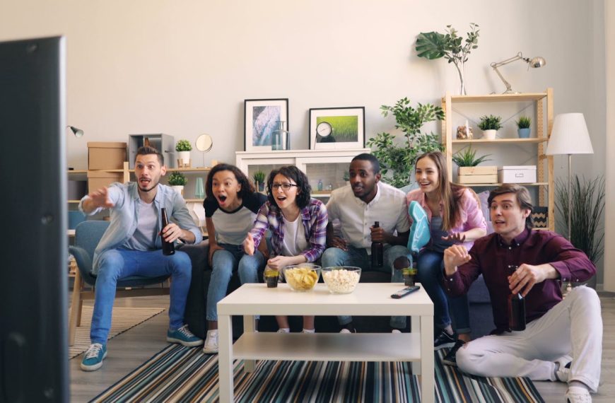 A lively group of diverse friends cheering while watching a sports game together in a cozy living room.