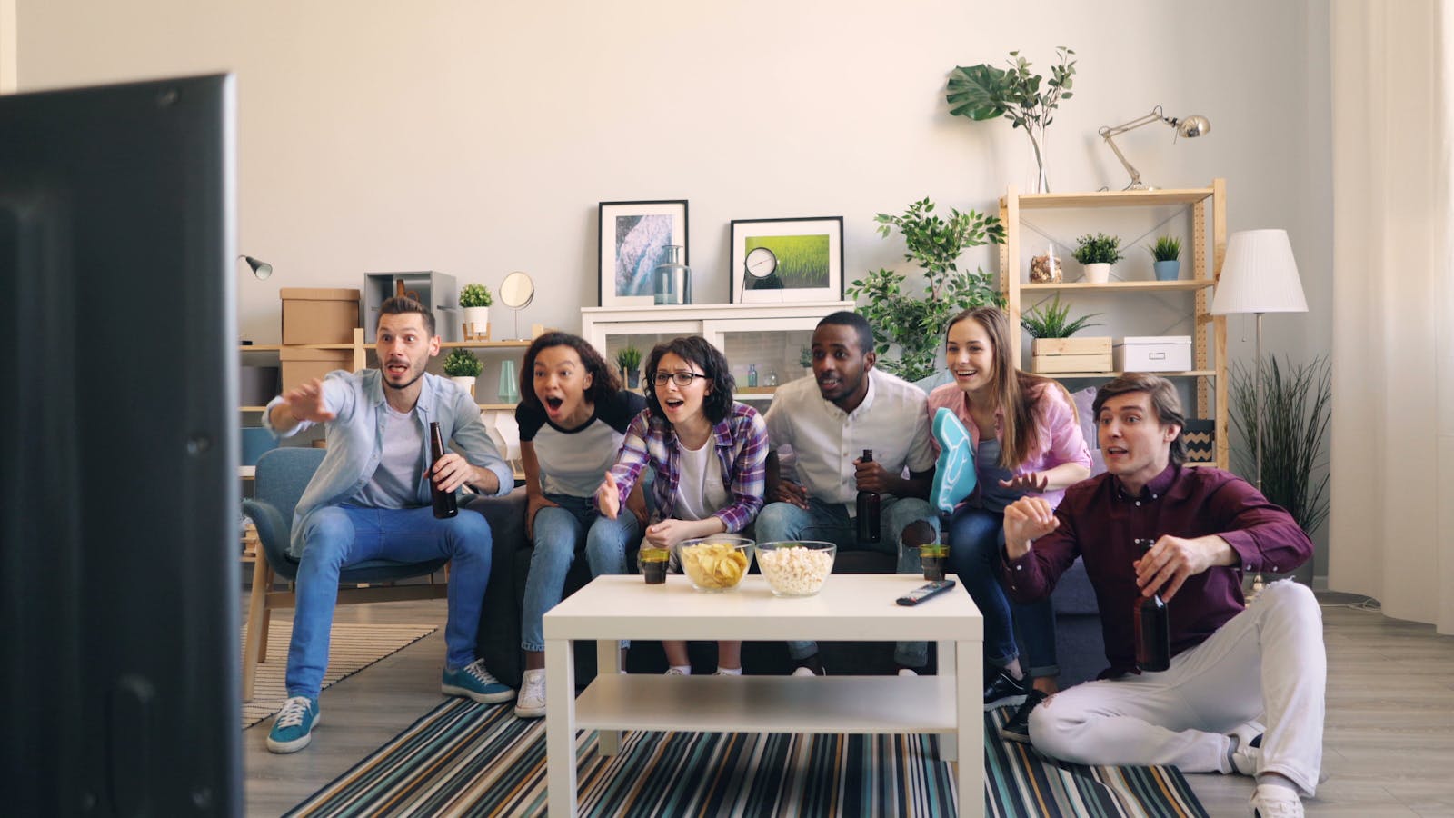 A lively group of diverse friends cheering while watching a sports game together in a cozy living room.