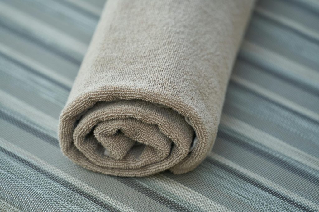 Close-up of a soft beige cotton towel rolled neatly on a striped fabric surface. Perfect for home decor or textile themes.
