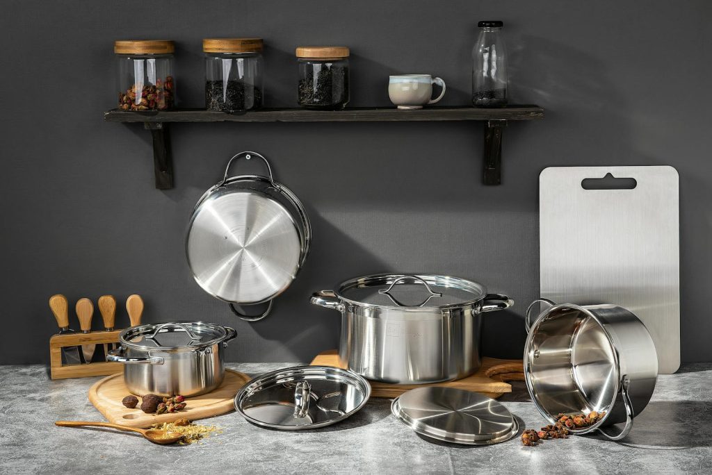 Stainless steel pots and kitchen essentials on concrete surface under shelf with jars.