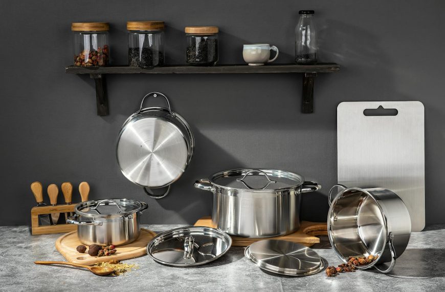 Stainless steel pots and kitchen essentials on concrete surface under shelf with jars.
