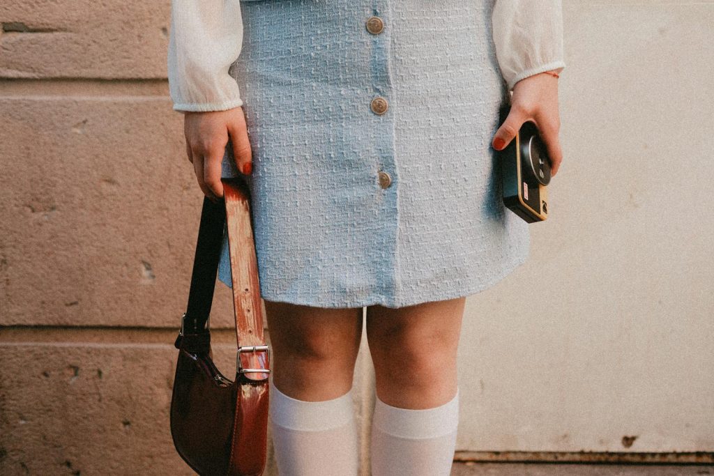 Stylish woman in retro outfit holding a vintage camera and handbag.