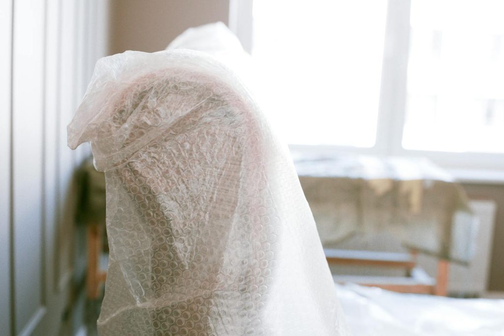 Furniture wrapped in bubble wrap for protection during a move in a bright sunlit room.