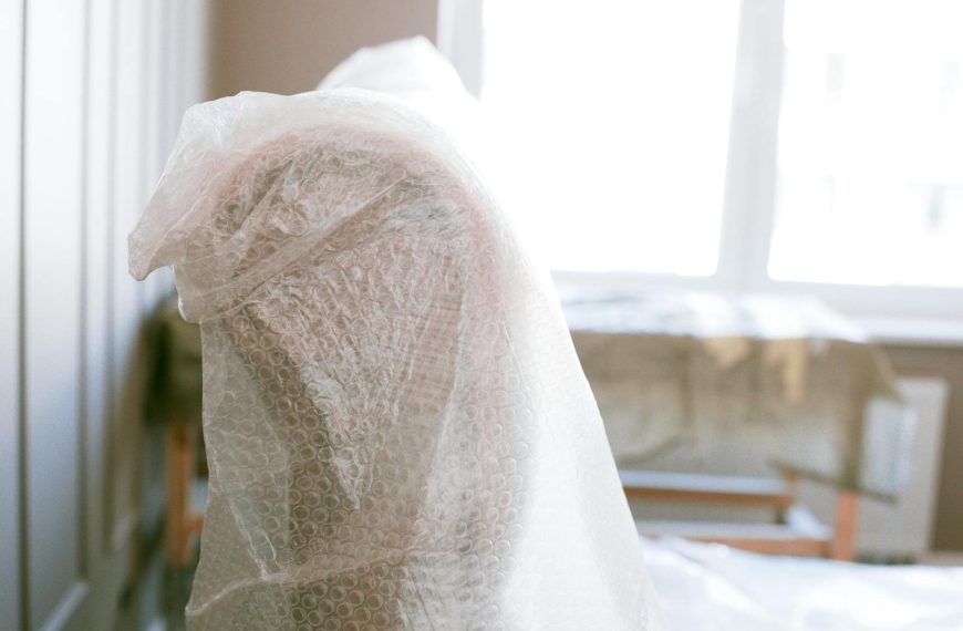 Furniture wrapped in bubble wrap for protection during a move in a bright sunlit room.