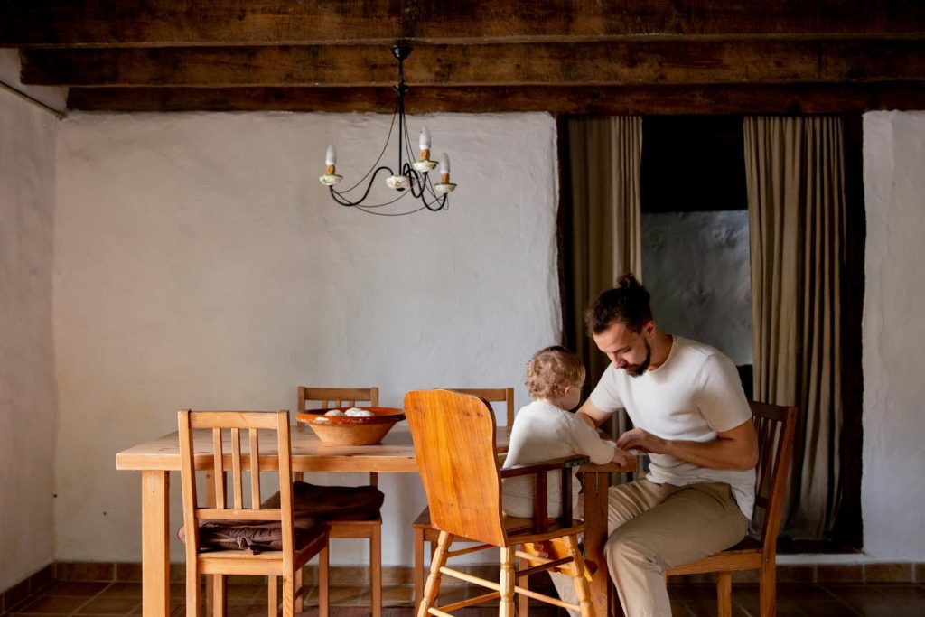 A father and child bonding together at a dining table in a rustic home interior.