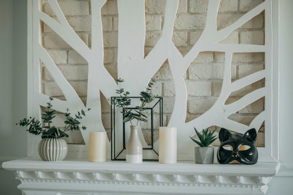A stylish mantel display featuring candles, vases, plants, and a decorative mask against a modern backdrop.