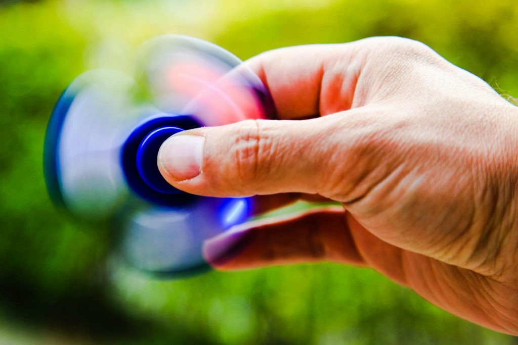 A person spins a fidget spinner outdoors, capturing the motion blur and vibrant colors.