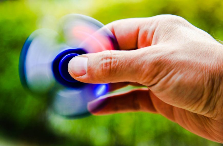A person spins a fidget spinner outdoors, capturing the motion blur and vibrant colors.