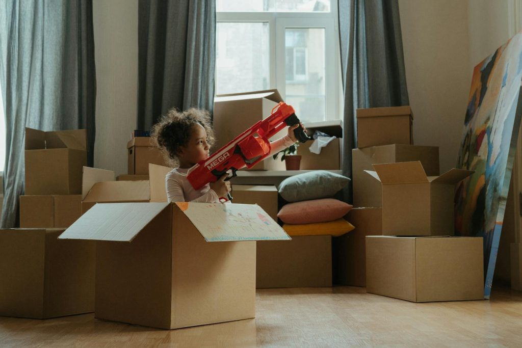 A child enjoying playtime with a toy gun amidst moving boxes, indoors.