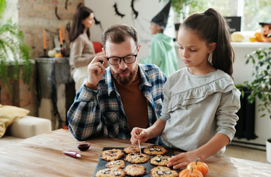 A father and daughter enjoy decorating Halloween cookies together in a cozy indoor setting.