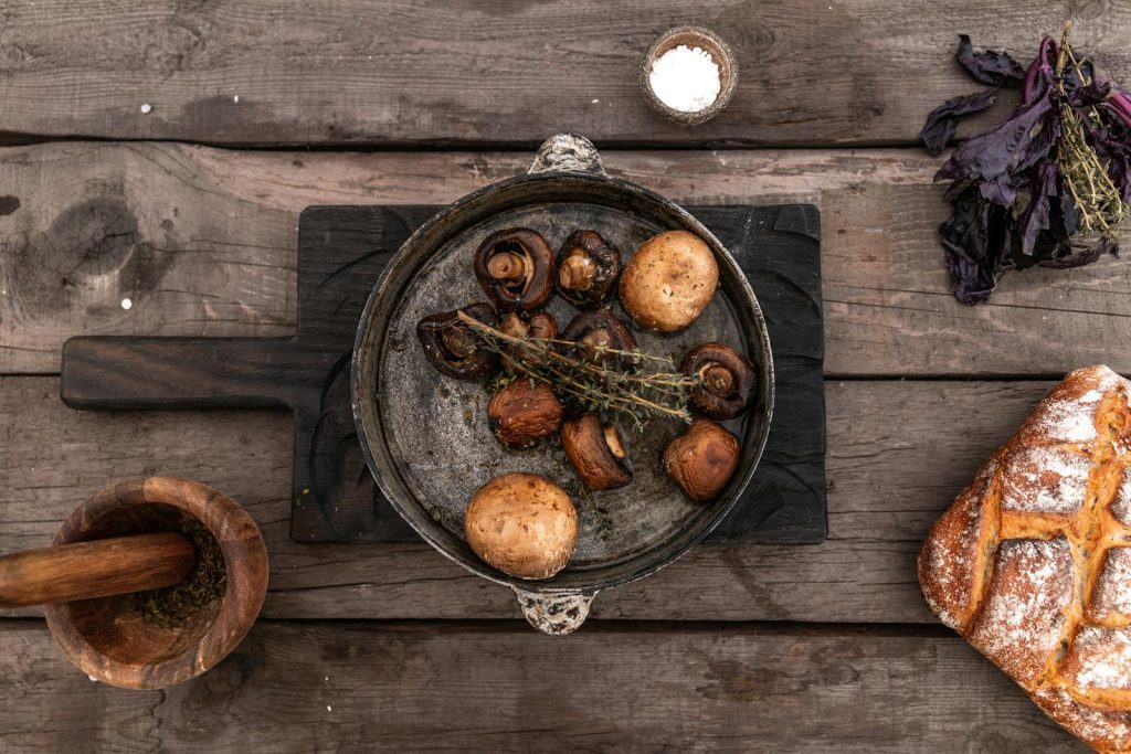 Top view of grilled mushrooms in a skillet with bread on a rustic wooden surface.