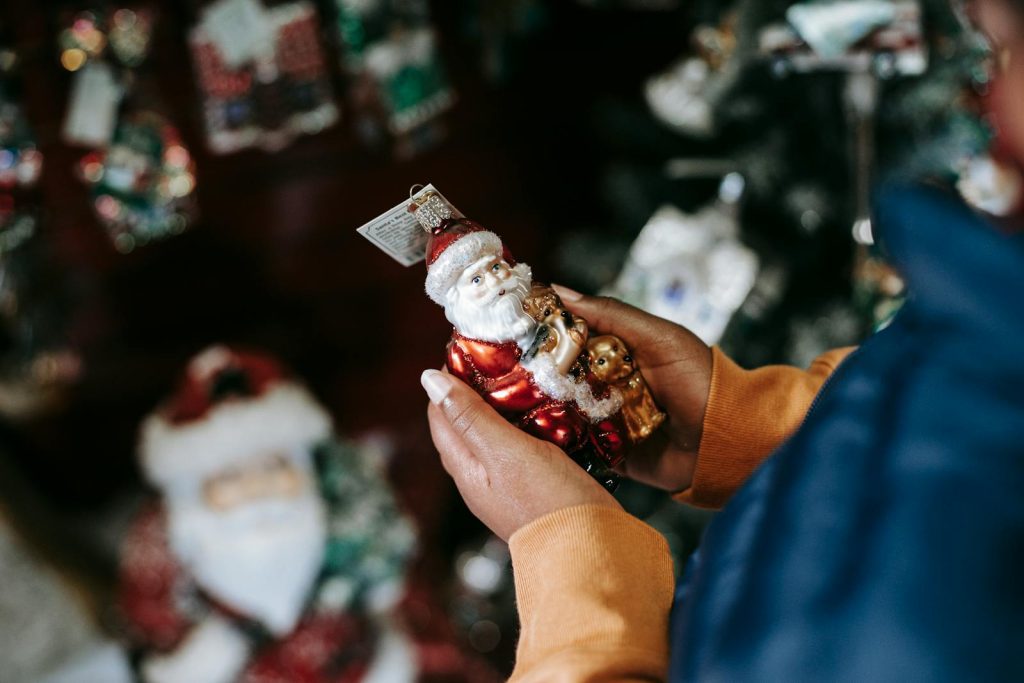 Close-up of hands holding a Santa Claus ornament in a festive holiday shop setting.