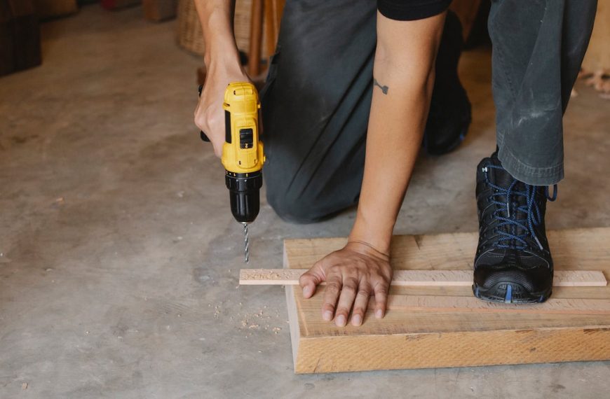 Close-up of a man using a drill on wooden planks in an indoor workshop.