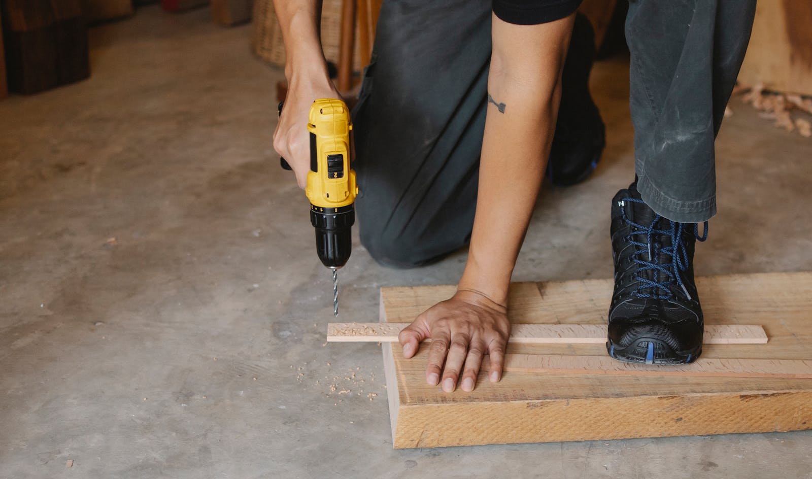 Close-up of a man using a drill on wooden planks in an indoor workshop.