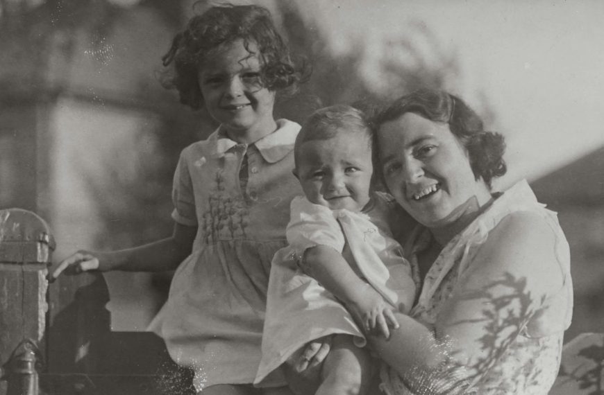 An old grayscale photo of a mother and her two children smiling outdoors.
