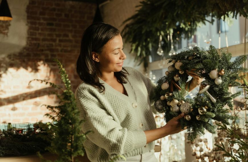 A woman admires a decorative Christmas wreath in a brightly lit room with festive holiday decor.