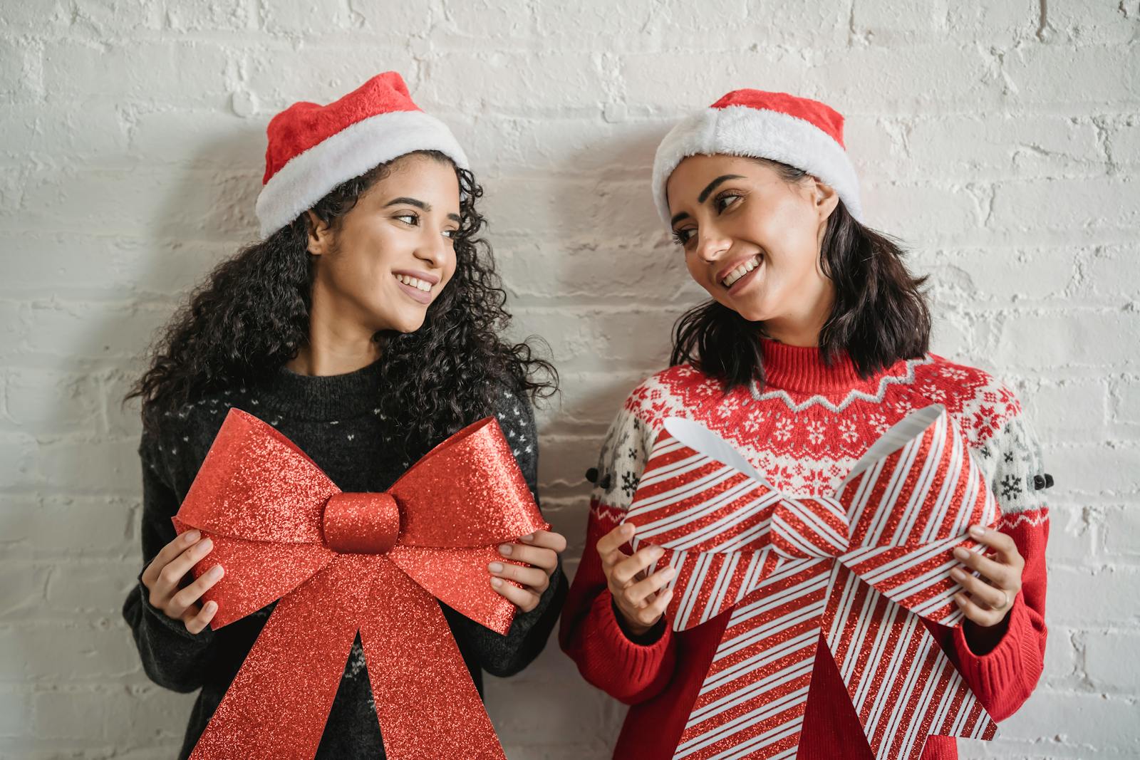 Happy young diverse women in Santa hats smiling and looking at each other while holding Christmas decoration