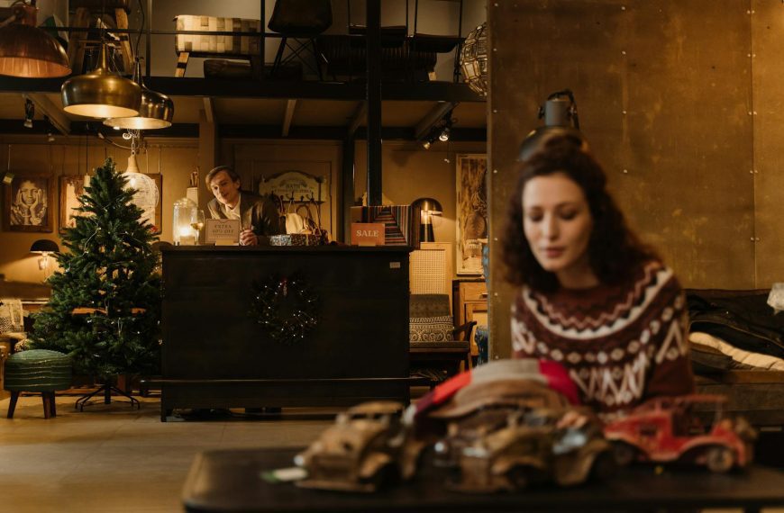 Woman shopping in a cozy store decorated for Christmas, with smiling salesman.
