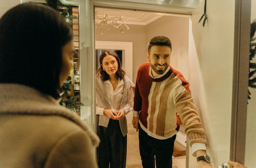 A couple greeting a guest at their doorway, capturing the warmth of a home during the holiday season.