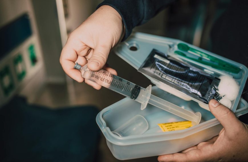 Close-up of a hand holding a syringe from a medical kit with various supplies.