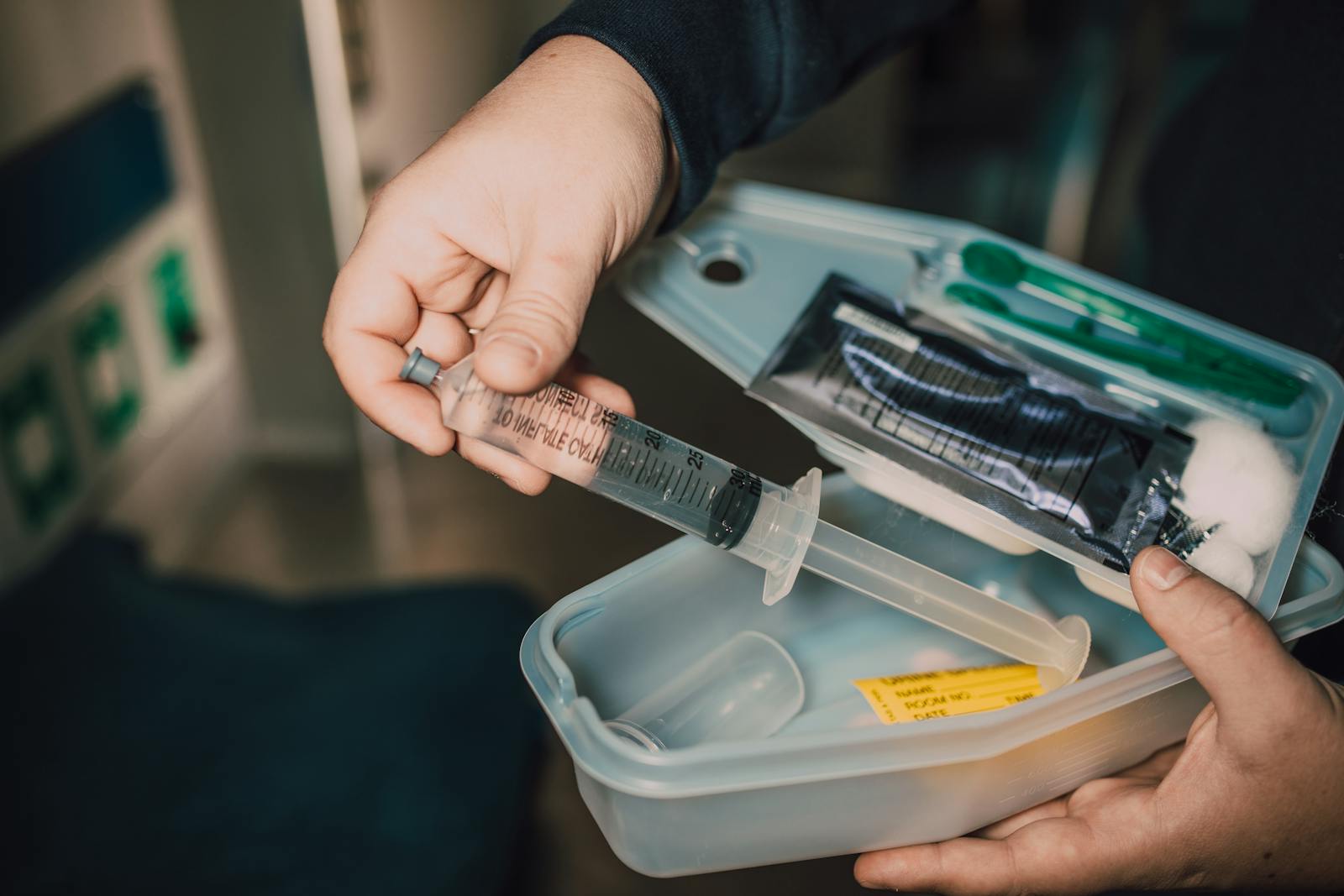Close-up of a hand holding a syringe from a medical kit with various supplies.