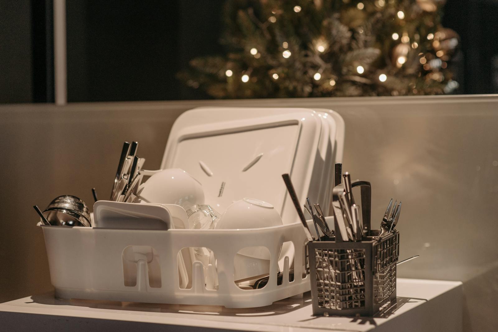 A dish rack with dishes and utensils beside a Christmas tree, creating a warm festive kitchen atmosphere.