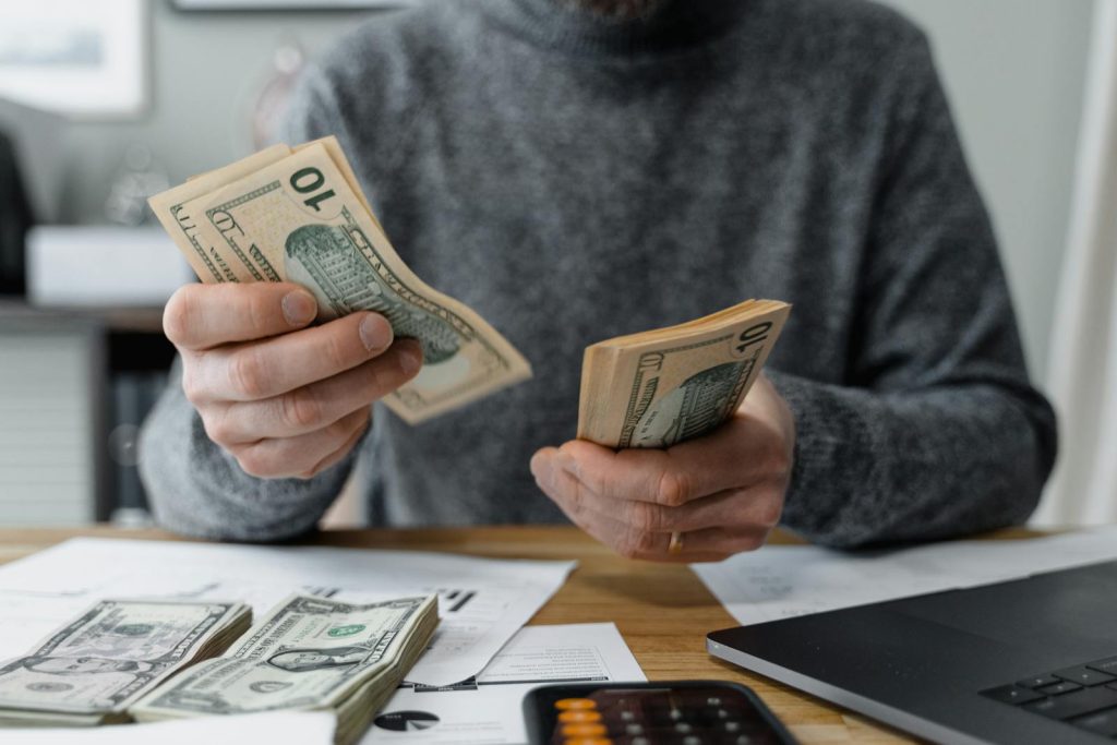 Close-up of person counting cash with a calculator and paperwork on a desk.