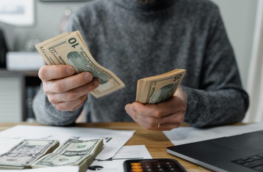Close-up of person counting cash with a calculator and paperwork on a desk.