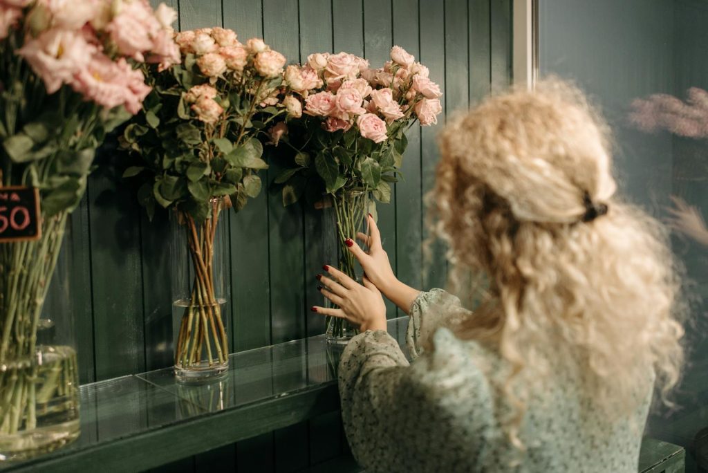 A florist arranges pink roses in vases on display in a flower shop.