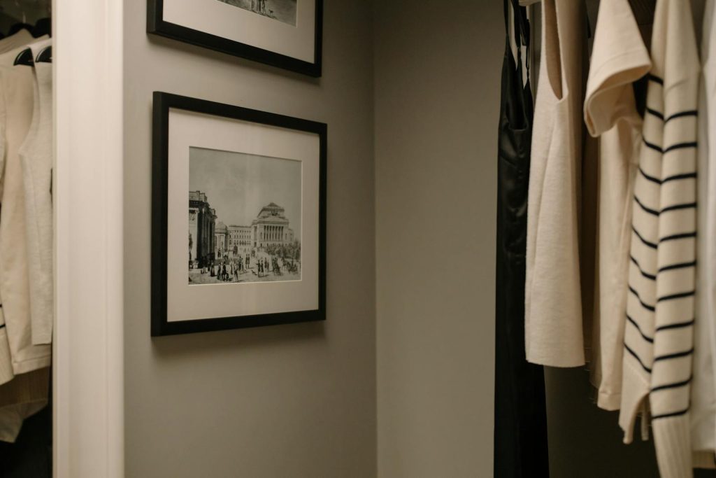 A well-organized closet with hanging clothes and vintage framed photographs for a modern minimalist look.