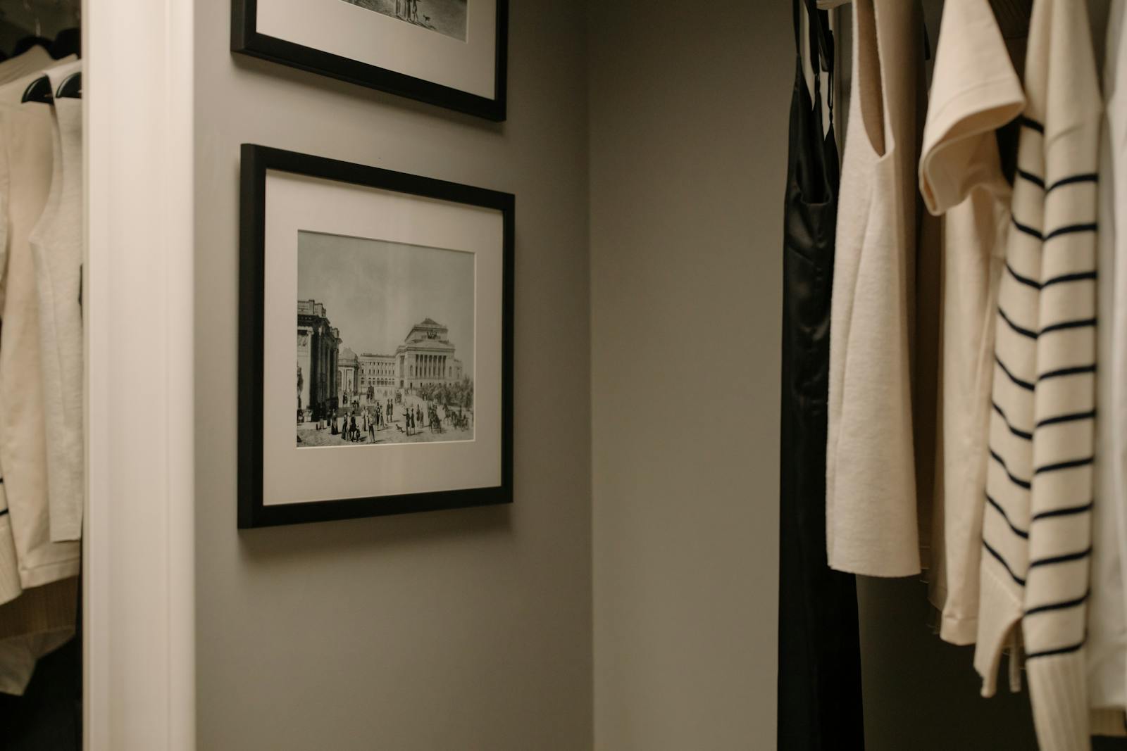 A well-organized closet with hanging clothes and vintage framed photographs for a modern minimalist look.