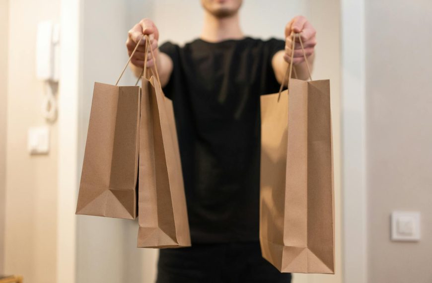 Adult holding several paper bags representing delivery service indoors.