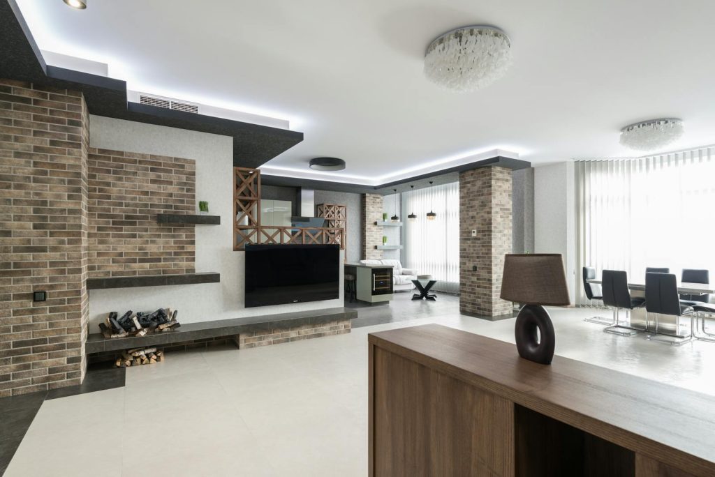 Modern TV at decorated wall in spacious living room with wooden cupboard in light apartment with table near big window