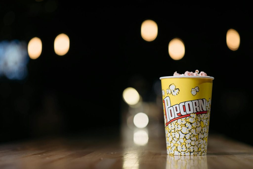 Close-up of popcorn in a yellow cup on a wooden table with blurred lights in the background, creating a cinematic ambiance.