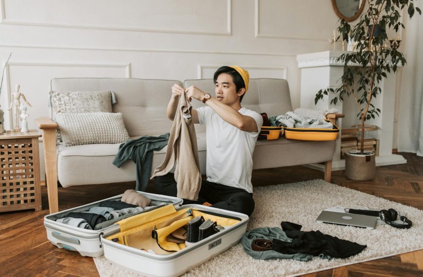 A young man organizes clothes into a suitcase in a stylish living room, preparing for a trip.