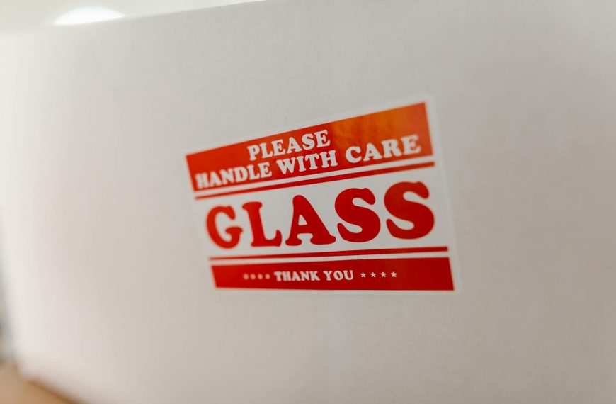 Close-up of a glass packaging label with 'Handle with Care' warning text on a white box.