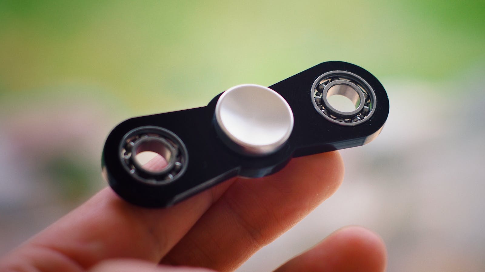Close-up view of a black fidget spinner held between fingers with a blurred background.