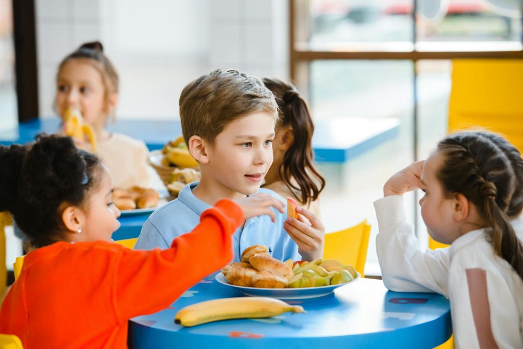 Group of diverse children enjoying a meal together indoors, fostering friendship and sharing.