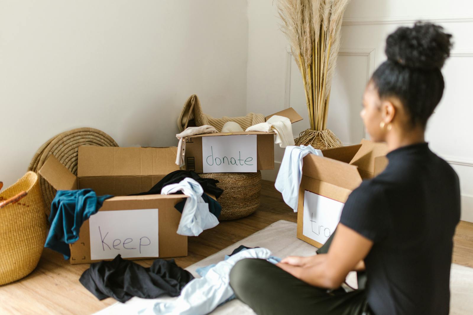 A woman organizing clothes into labeled boxes for donation and keeping.