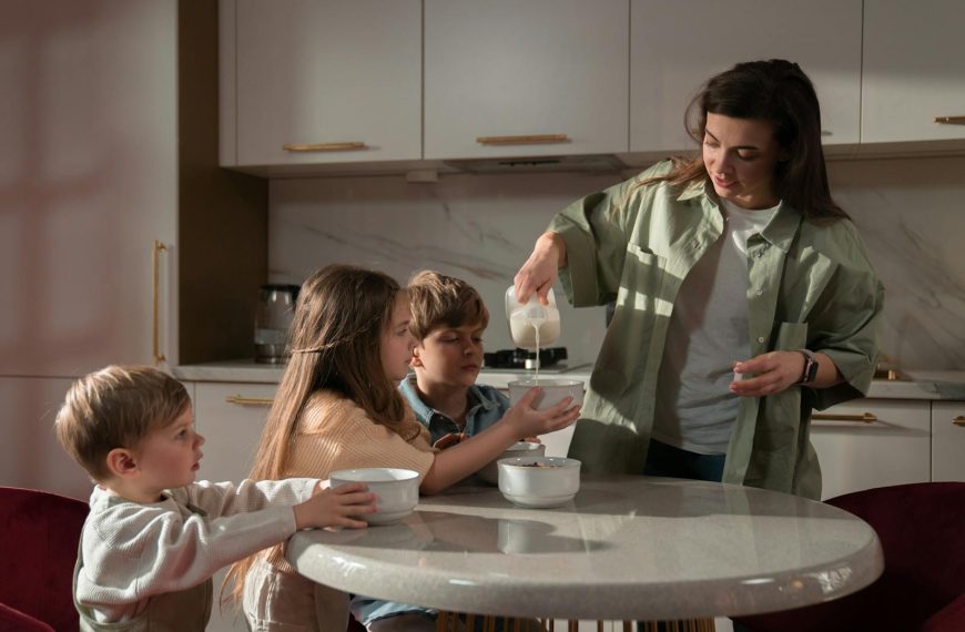 A mother pours milk into bowls for her three children during breakfast time at home.