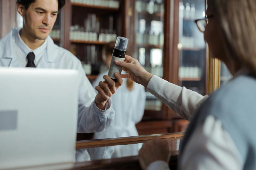 A pharmacist in a white uniform hands medication to a customer across the counter.