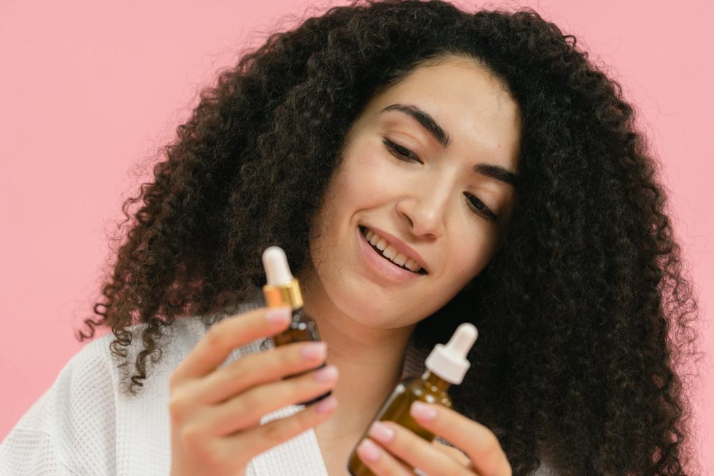 A young woman analyzes skincare bottles, set against a pink backdrop.