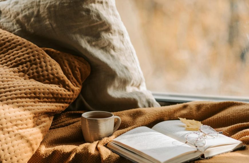 Inviting autumn scene with book, eyewear, and a warm drink by a window, perfect for relaxation.